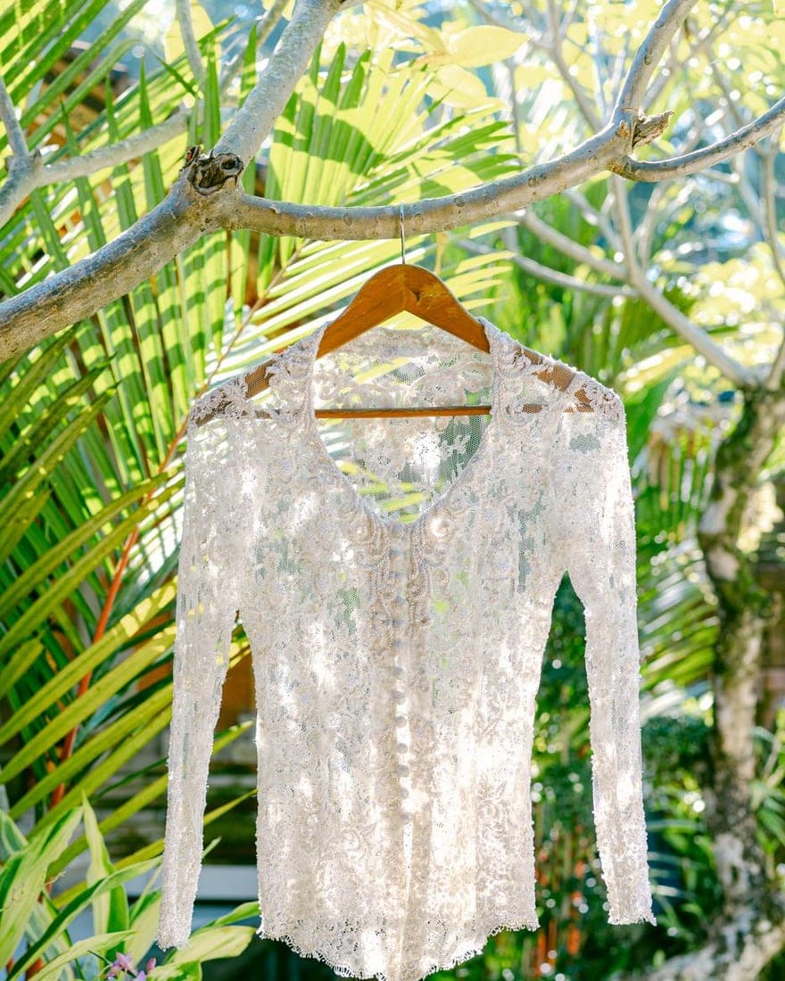 Blusa de encaje blanco colgada de la rama de un árbol, con fondo de plantas