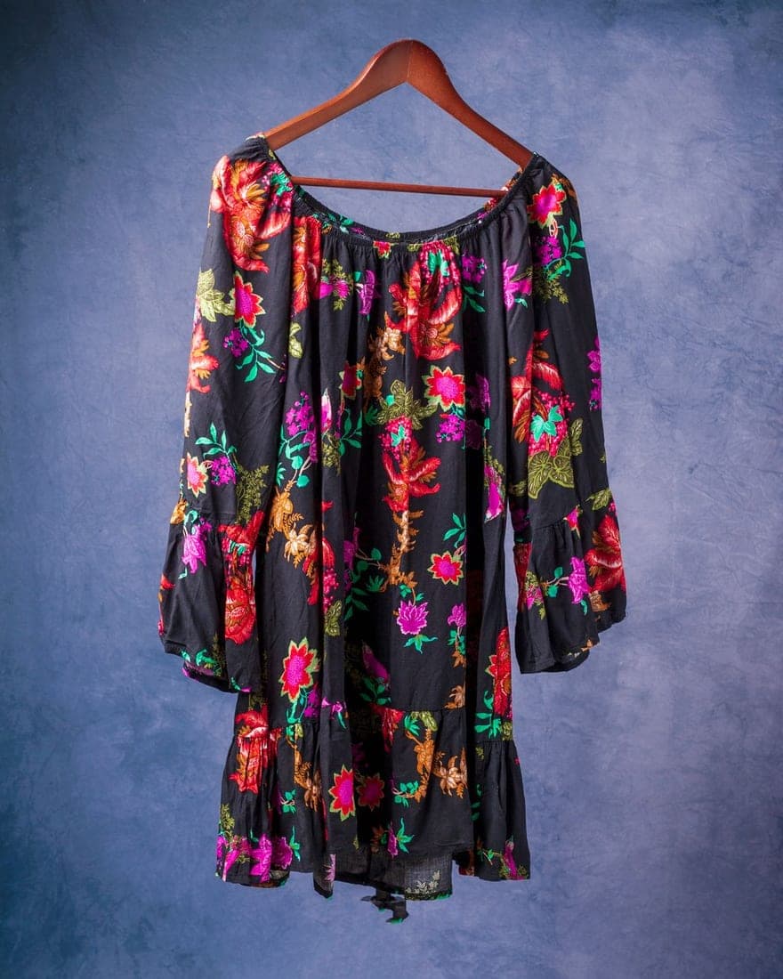 Blusa negra con estampado floral colgada en una percha de madera contra una pared azul